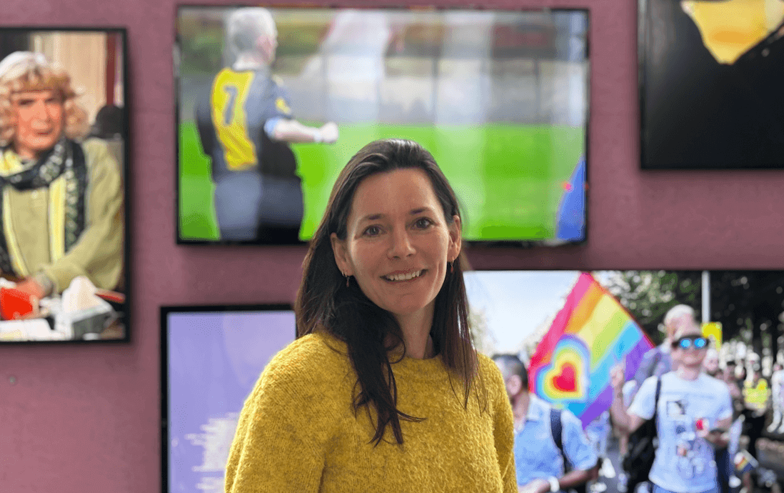 Portretfoto van Valentine Kuypers voor een roze wand waarop meerdere tv-schermen zijn gemonteerd met verschillende beelden