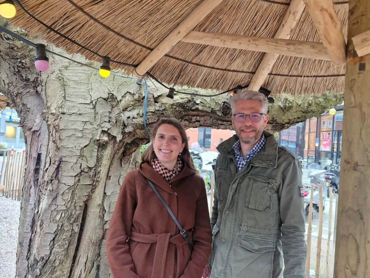 Portretfoto van Merel Geerlings en Sjors de Valk onder een rieten parasol voor een grote boom