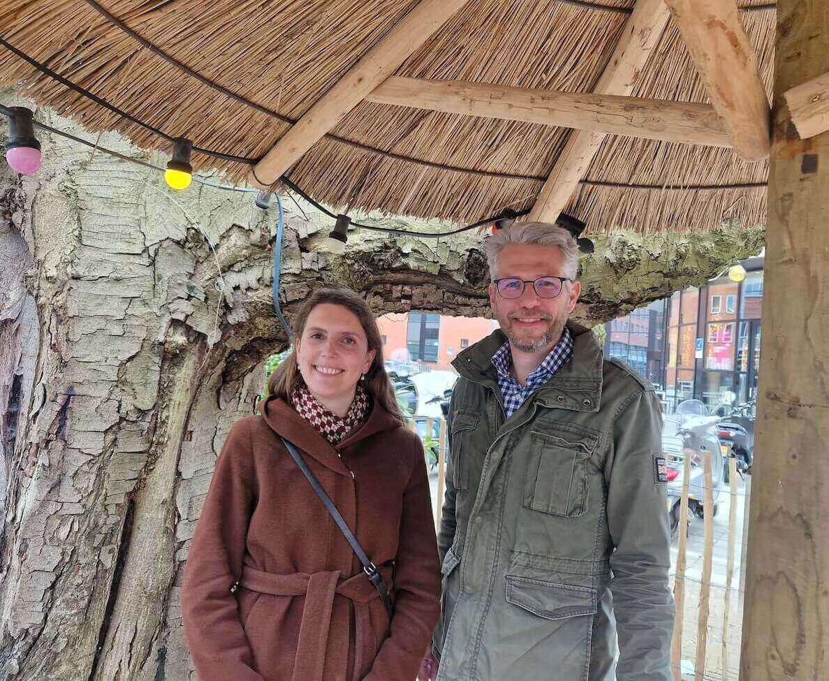 Portretfoto van Merel Geerlings en Sjors de Valk onder een rieten parasol voor een grote boom